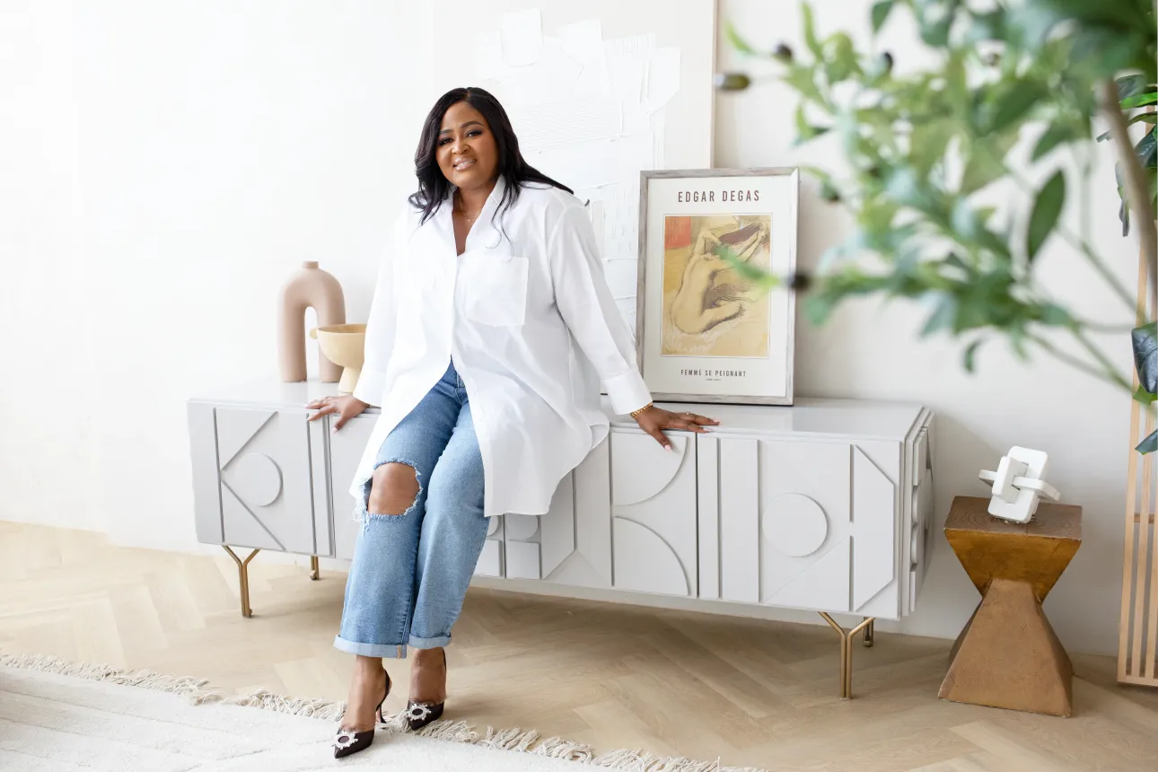 Woman in white shirt and ripped jeans sitting on a modern white sideboard.